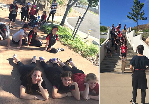 Secondary school students walking, sitting and laying on a pathway in a garden setting. Others stand waiting on at the top of a flight of steps looking down at a performance director who stands facing them. 