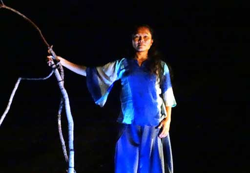 Dancer Alla stands waiting with branch staff in hand at the site of 'gathering'—during a performance.