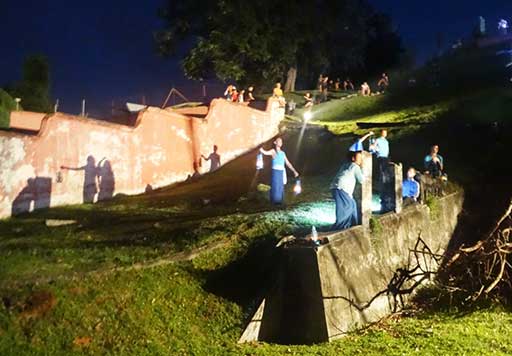 Performers gather on a hillside while audience members look on from above.